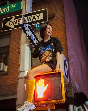 Williamsburg New York USA 14 June 2026 View of a young woman celebrating the NBA championship victory while sitting on a pedestrian traffic signal at night. Williamsburg New York USA 14 June 2026 View of a young woman celebrating the NBA championship victory while sitting on a pedestrian traffic signal at night.