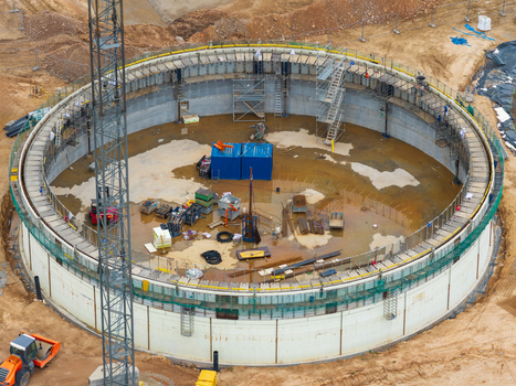 Aerial view of a large circular construction site featuring concrete walls scaffolding a tall crane and various equipment on the ground in Lithuania. Aerial view of a large circular construction site featuring concrete walls scaffolding a tall crane and various equipment on the ground in Lithuania.