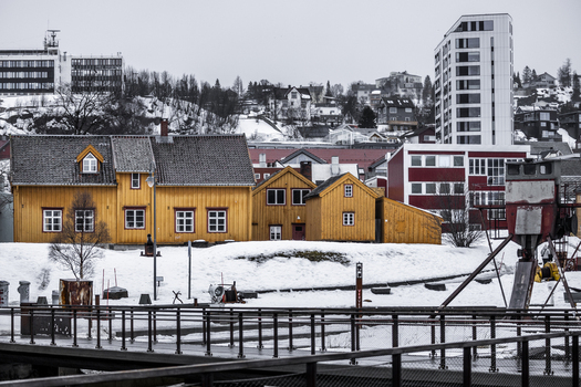 View of traditional yellow wooden houses nestled in a snowy landscape with modern architecture and hills in the background Tromso Troms Norway. View of traditional yellow wooden houses nestled in a snowy landscape with modern architecture and hills in the background Tromso Troms Norway.