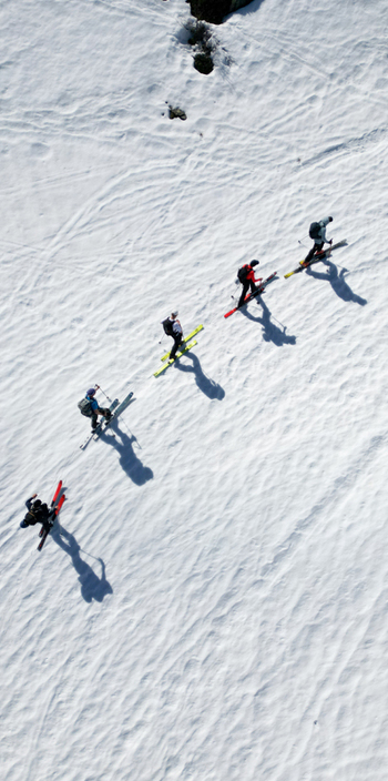 Aerial view of a group of ski tourers ascending the snowy slopes of Pointe Ronde casting long shadows on the textured white snow Trient Valais Switzerland.