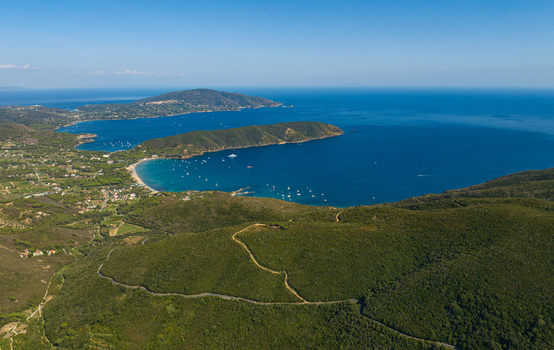 Aerial view of Lacona Beach with its sandy coastline turquoise waters and numerous boats anchored in the bay surrounded by lush green hills in Lacona Tuscany Italy.