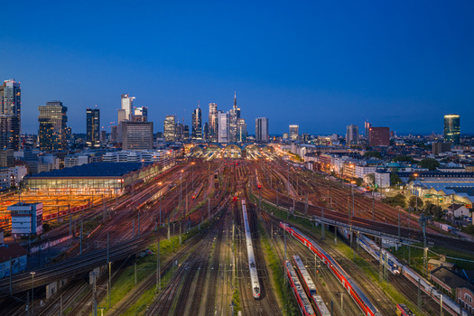 Aerial view of Hauptbahnhof with numerous railway tracks and trains leading towards the illuminated city skyline at dusk in Frankfurt am Main Hessen Germany.
