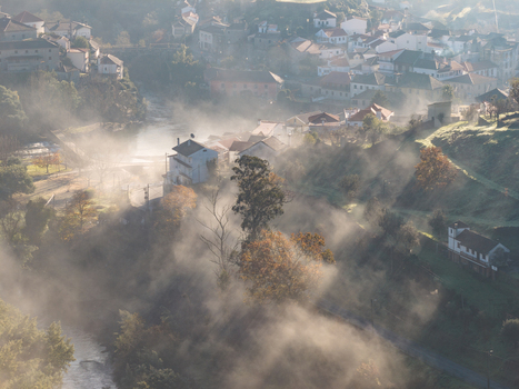 Aerial view of the historic village of Avo shrouded in morning mist with sunlight rays piercing through the fog and lush green hills Oliveira do Hospital Coimbra District Portugal.