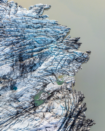Aerial view of a glacier with deep crevasses textured ice formations and meltwater pools meeting the glacial lake in Iceland. Aerial view of a glacier with deep crevasses textured ice formations and meltwater pools meeting the glacial lake in Iceland.