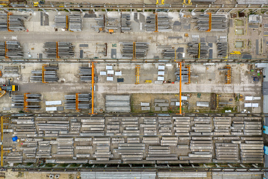 Aerial view of prestressed concrete elements production yard with rows of stacked beams industrial overhead cranes and organized storage areas in Poland.