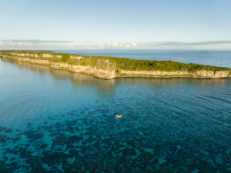 Aerial view of turquoise waters meet the verdant cliffs of the island a lone boat adrift in the serene expanse Ouvéa Loyalty Islands Province New Caledonia. Aerial view of turquoise waters meet the verdant cliffs of the island a lone boat adrift in the serene expanse Ouvéa Loyalty Islands Province New Caledonia.