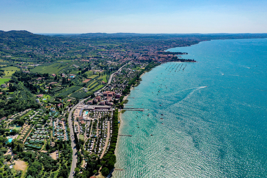 Aerial view of the turquoise waters and lush green coastline of Lake Garda with a coastal road and small boats in Italy. Aerial view of the turquoise waters and lush green coastline of Lake Garda with a coastal road and small boats in Italy.