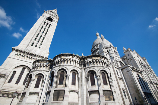 View of the white stone facade domes and bell tower of the Basilique du Sacre Coeur de Montmartre under a clear blue sky in Paris Ile de France France. View of the white stone facade domes and bell tower of the Basilique du Sacre Coeur de Montmartre under a clear blue sky in Paris Ile de France France.