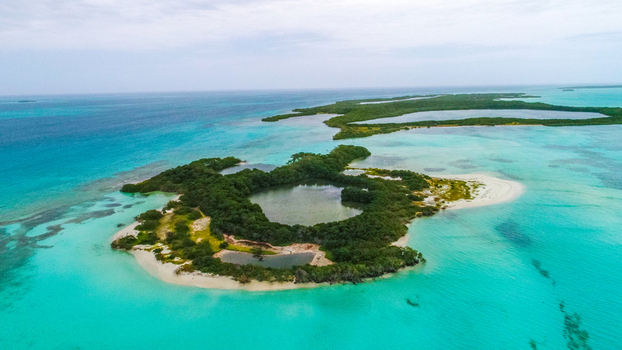 Aerial view of Los Roques archipelago featuring a lush green island with a central lagoon surrounded by vibrant turquoise Caribbean waters and white sandy beaches in Los Roques Dependencias Federale Venezuela. Aerial view of Los Roques archipelago featuring a lush green island with a central lagoon surrounded by vibrant turquoise Caribbean waters and white sandy beaches in Los Roques Dependencias Federale Venezuela.