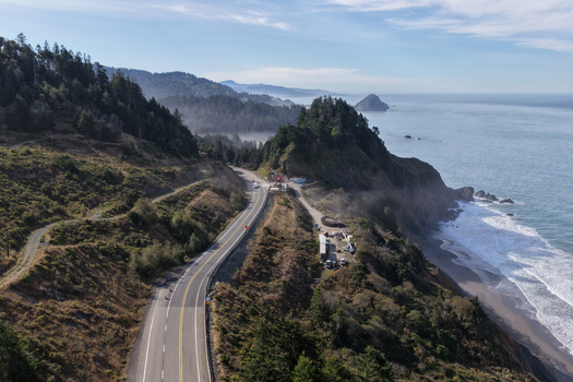 Aerial view of Highway 101 winding along the rugged cliffs of the southern Oregon coast with the Pacific Ocean and forest landscape in Port Orford Oregon United States. Aerial view of Highway 101 winding along the rugged cliffs of the southern Oregon coast with the Pacific Ocean and forest landscape in Port Orford Oregon United States.