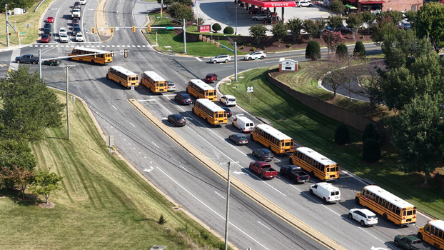 Aerial view of a line of yellow school buses waiting at an intersection with surrounding green lawns and traffic in Forest Virginia United States. Aerial view of a line of yellow school buses waiting at an intersection with surrounding green lawns and traffic in Forest Virginia United States.