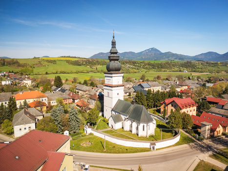 Aerial view of St. Matthew s Church with its tall white tower and dark dome surrounded by village houses green meadows and distant mountains in Partizanska Lupca Zilina Region Slovakia. Aerial view of St. Matthew s Church with its tall white tower and dark dome surrounded by village houses green meadows and distant mountains in Partizanska Lupca Zilina Region Slovakia.