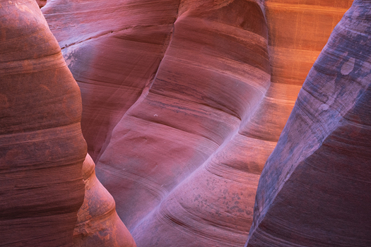 View of smooth layered sandstone walls curve and glow with warm light in a narrow slot canyon creating a surreal and inviting space Escalante Utah United States.