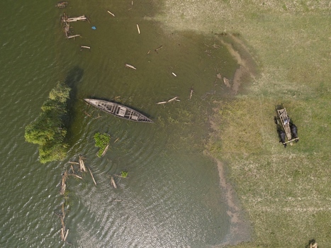 Aerial view of a traditional wooden boat moored near the grassy riverbank where a cart pulled by water buffalo is moving along the shore in Kushtia Khulna Division Bangladesh. Aerial view of a traditional wooden boat moored near the grassy riverbank where a cart pulled by water buffalo is moving along the shore in Kushtia Khulna Division Bangladesh.