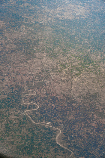 Aerial view of a winding river meandering through a vast landscape of agricultural fields and rural settlements under a hazy sky in India. Aerial view of a winding river meandering through a vast landscape of agricultural fields and rural settlements under a hazy sky in India.