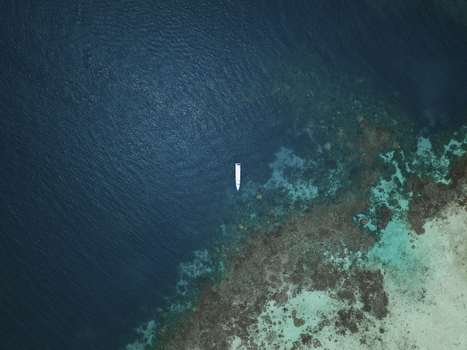 Aerial view of a lone boat adrift on the deep blue sea contrasting with the vibrant turquoise shallows near the coral reefs Karimunjawa Central Java Indonesia.