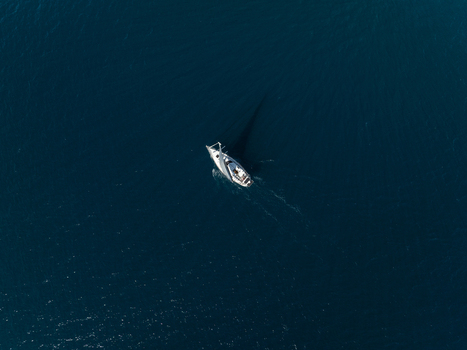 Aerial view of a white sailboat cruising through the deep blue waters of the Mediterranean Sea with a gentle wake Plemmirio Sicily Italy. Aerial view of a white sailboat cruising through the deep blue waters of the Mediterranean Sea with a gentle wake Plemmirio Sicily Italy.