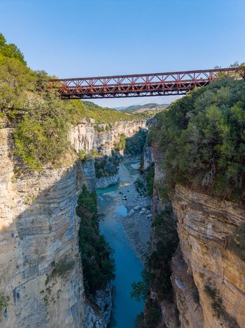 Aerial view of Osumi canyon featuring a metal bridge spanning the deep rocky gorge with a turquoise river flowing below surrounded by lush greenery in Dhores Berat County Albania.