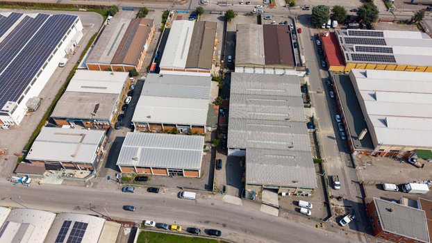 Aerial view of an industrial and logistics complex with multiple warehouses metal roofs solar panels and surrounding access roads in San Giuliano Milanese Lombardy Italy. Aerial view of an industrial and logistics complex with multiple warehouses metal roofs solar panels and surrounding access roads in San Giuliano Milanese Lombardy Italy.