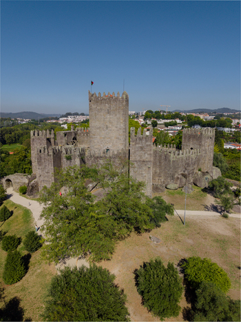 Aerial view of the historic Guimaraes Castle with its stone walls and battlements surrounded by lush greenery under a clear blue sky in Guimaraes Braga Portugal. Aerial view of the historic Guimaraes Castle with its stone walls and battlements surrounded by lush greenery under a clear blue sky in Guimaraes Braga Portugal.