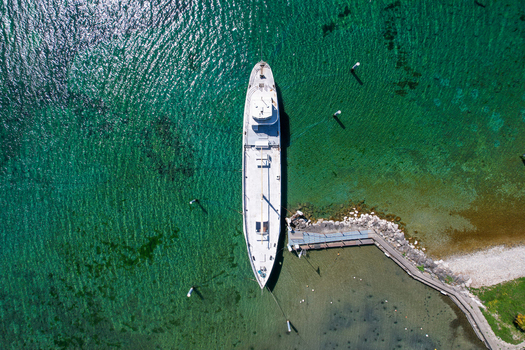 Aerial view of a white ship docked at a small stone pier on the clear turquoise waters of Lake Geneva in Perroy Vaud Switzerland. Aerial view of a white ship docked at a small stone pier on the clear turquoise waters of Lake Geneva in Perroy Vaud Switzerland.