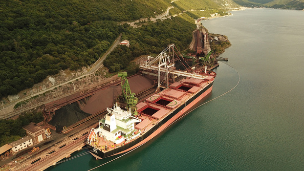 Aerial view of a large bulk carrier ship docked at a port facility with industrial cranes loading cargo near a forested coastline in Bakarac Primorje Gorski Kotar Croatia. Aerial view of a large bulk carrier ship docked at a port facility with industrial cranes loading cargo near a forested coastline in Bakarac Primorje Gorski Kotar Croatia.