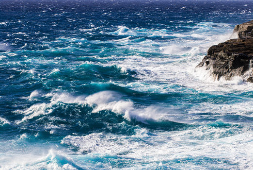 View of powerful turquoise ocean waves crashing against the rugged volcanic rock cliffs of the South Shore in Oahu Hawaii United States.