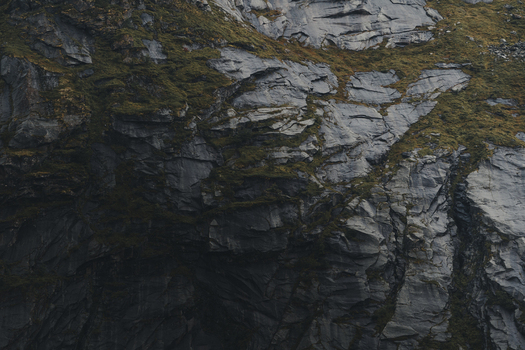 View of the rugged dark rocky cliff face of Lofoten with patches of green moss and textured stone surfaces Nordland Norway.