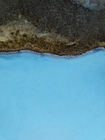 Aerial view of the milky blue geothermal waters of the Reykjanes peninsula contrasting with dark volcanic terrain in Grindavikurbaer Iceland. Aerial view of the milky blue geothermal waters of the Reykjanes peninsula contrasting with dark volcanic terrain in Grindavikurbaer Iceland.