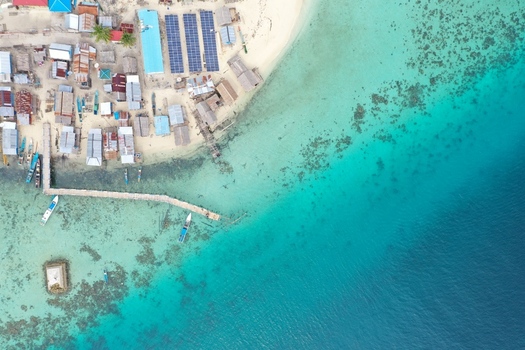 Aerial view of Pulau Maginti coastal village with solar panels a wooden pier and traditional boats moored in the turquoise waters of the coral reef in Maginti South East Sulawesi Indonesia.