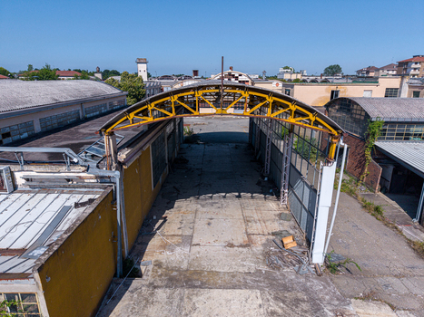 Aerial view of an abandoned industrial warehouse with a yellow metal arch weathered concrete flooring and old factory buildings in Casale Monferrato Piedmont Italy. Aerial view of an abandoned industrial warehouse with a yellow metal arch weathered concrete flooring and old factory buildings in Casale Monferrato Piedmont Italy.
