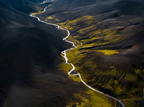 Aerial view of a river meandering through dark volcanic landscape contrasted by vibrant green vegetation creating a surreal untouched panorama Iceland. Aerial view of a river meandering through dark volcanic landscape contrasted by vibrant green vegetation creating a surreal untouched panorama Iceland.