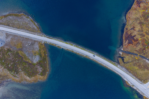 Aerial view of a road crossing a narrow strait between rocky landmasses with autumn vegetation in Skjak Innlandet Norway.