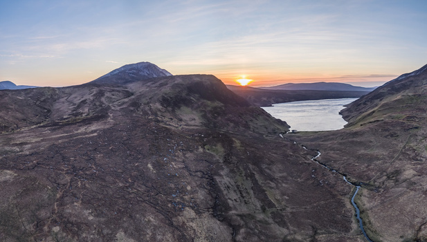 Aerial view of Altan Lough at sunset featuring rugged mountain slopes a winding stream and golden light over the landscape in County Donegal Ireland.