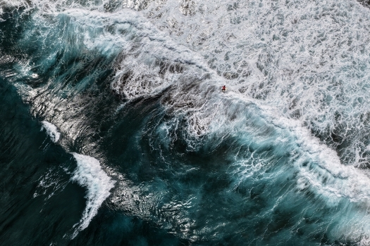 Aerial view of a surfer riding a massive crashing wave with white foam and deep blue water at Praia do Areal de Santa Barbara in Ribeira Grande Acores Portugal. Aerial view of a surfer riding a massive crashing wave with white foam and deep blue water at Praia do Areal de Santa Barbara in Ribeira Grande Acores Portugal.