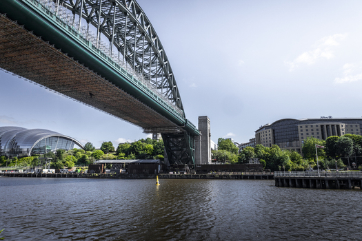 View of the Tyne Bridge spanning the River Tyne with the Sage Gateshead music centre visible in the background under a clear blue sky in Newcastle upon Tyne England United Kingdom. View of the Tyne Bridge spanning the River Tyne with the Sage Gateshead music centre visible in the background under a clear blue sky in Newcastle upon Tyne England United Kingdom.