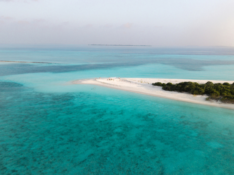 Aerial view of a serene island with white sands meeting turquoise waters framed by lush greenery under a soft sky Dhidhdhoo Thiladhunmathi Atoll Maldives.