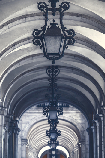 View of the ornate iron lanterns hanging from the vaulted stone arches of the arcade at Praca do Comercio Lisbon Lisbon Portugal.