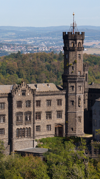 Aerial view of the historic stone architecture of Schaumburg Castle with its prominent tower surrounded by lush green forests and rolling hills in Balduinstein Rheinland Pfalz Germany. Aerial view of the historic stone architecture of Schaumburg Castle with its prominent tower surrounded by lush green forests and rolling hills in Balduinstein Rheinland Pfalz Germany.