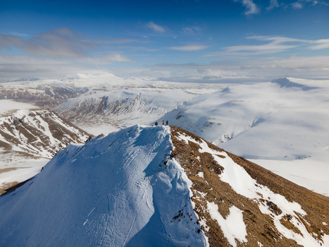 Aerial view of Moskardhshnukar mountain peak with hikers standing on the snowy summit overlooking a vast winter landscape under a blue sky Mosfellsbaer Kjosarhreppur Iceland. Aerial view of Moskardhshnukar mountain peak with hikers standing on the snowy summit overlooking a vast winter landscape under a blue sky Mosfellsbaer Kjosarhreppur Iceland.