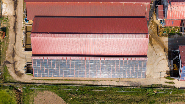 Aerial view of a dairy farm with red metal roofs and large solar panel arrays installed on the building surrounded by rural fields in San Giuliano Milanese Lombardy Italy. Aerial view of a dairy farm with red metal roofs and large solar panel arrays installed on the building surrounded by rural fields in San Giuliano Milanese Lombardy Italy.
