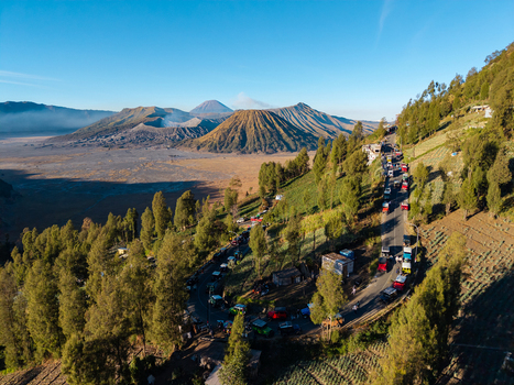 Kecamatan Puspo Jawa Timur Indonesia 08 August 2026 Aerial view of Seruni Point overlooking Mount Bromo volcanic landscape with a winding road tourist vehicles and green hillsides.