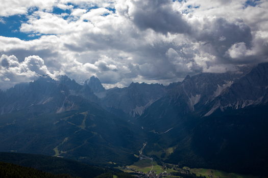 View of the jagged peaks of the Dolomites under a dramatic cloudy sky overlooking a lush green valley and small village in Rocca Pietore Veneto Italy. View of the jagged peaks of the Dolomites under a dramatic cloudy sky overlooking a lush green valley and small village in Rocca Pietore Veneto Italy.