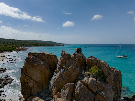 Aerial view of Castle Rock with two people sitting on the granite formation overlooking turquoise waters a sailboat and the coastline of Dunsborough Western Australia Australia. Aerial view of Castle Rock with two people sitting on the granite formation overlooking turquoise waters a sailboat and the coastline of Dunsborough Western Australia Australia.