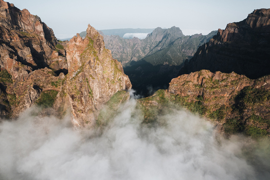 Aerial view of jagged peaks piercing through a sea of clouds the rugged landscape painted in warm hues against the soft ethereal mist Pico do Areeiro Madeira Portugal.