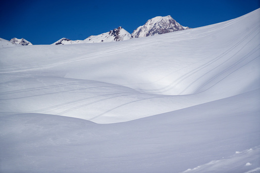 Aerial view of the snow covered slopes of Colle del Piccolo San Bernardo with ski tracks and mountain peaks under a clear blue sky in La Thuile Valle d Aosta Italy. Aerial view of the snow covered slopes of Colle del Piccolo San Bernardo with ski tracks and mountain peaks under a clear blue sky in La Thuile Valle d Aosta Italy.