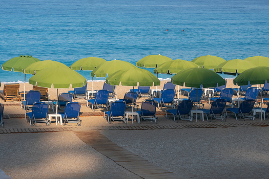 View of rows of bright green umbrellas create a playful contrast against the deep blue sea and sky with blue beach chairs in Kathisma Lefkada Greece. View of rows of bright green umbrellas create a playful contrast against the deep blue sea and sky with blue beach chairs in Kathisma Lefkada Greece.