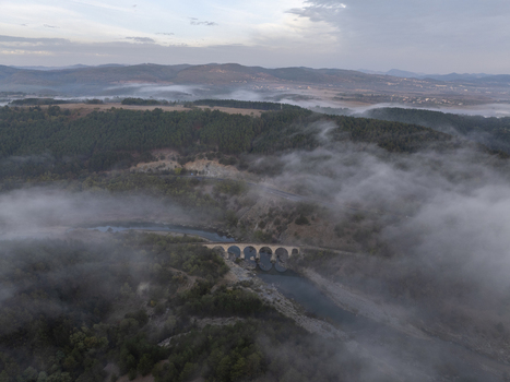 Aerial view of the historic stone railway bridge spanning a river amidst rolling hills and dense forests partially obscured by thick morning mist Balabanovo Kardzhali Province Bulgaria. Aerial view of the historic stone railway bridge spanning a river amidst rolling hills and dense forests partially obscured by thick morning mist Balabanovo Kardzhali Province Bulgaria.