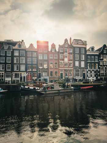 View of historic canal houses with traditional gabled facades and boats moored on the water under a soft sunset sky Amsterdam North Holland Netherlands. View of historic canal houses with traditional gabled facades and boats moored on the water under a soft sunset sky Amsterdam North Holland Netherlands.