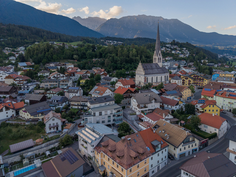Aerial view of the alpine town featuring a historic church traditional houses with red tiled roofs and lush mountain valley scenery in Imst Tyrol Austria.